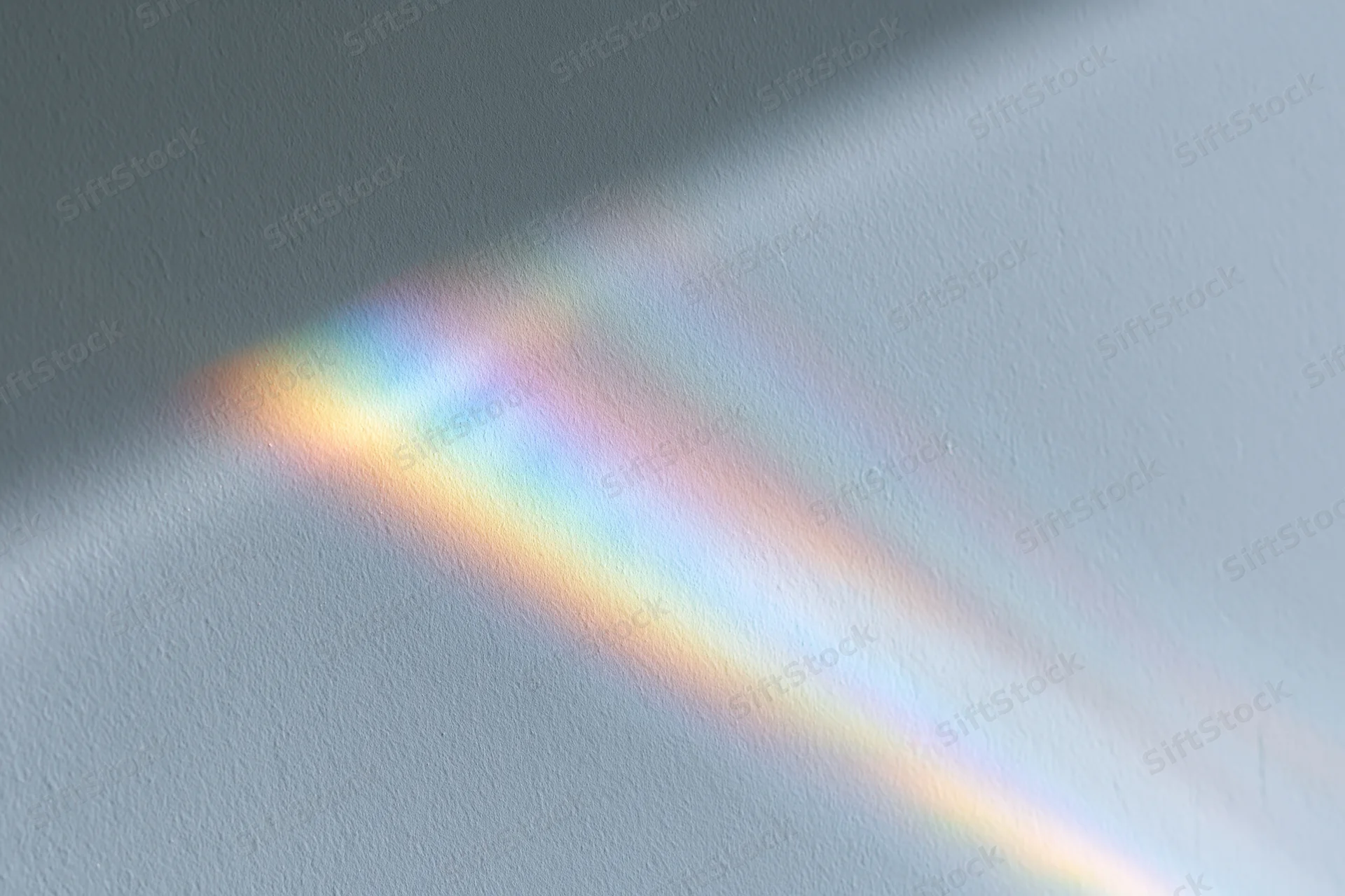Rainbow light refraction cast across a pale grey-white wall surface