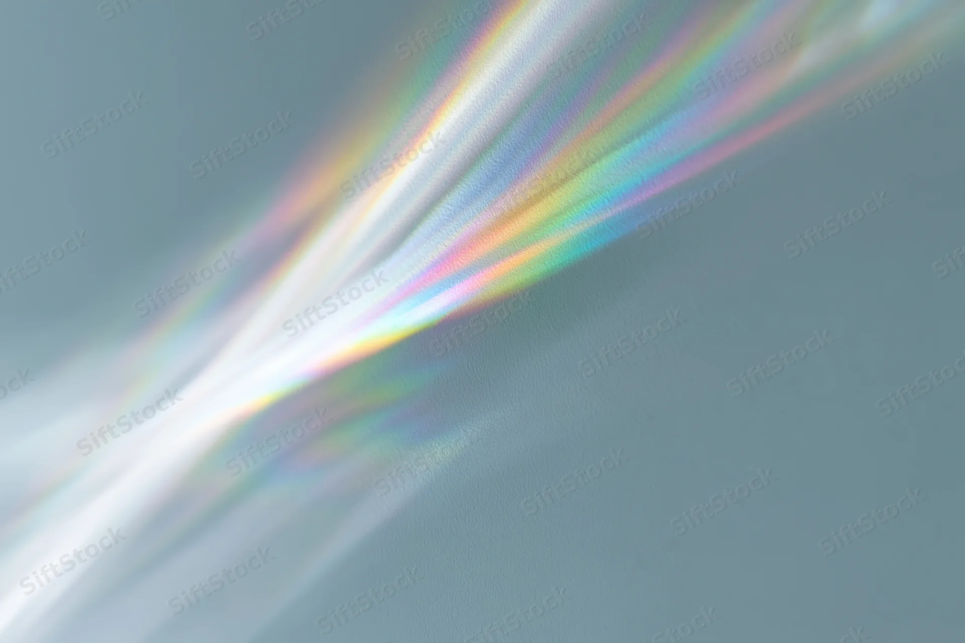 Rainbow light refraction cast across a pale grey-white wall surface