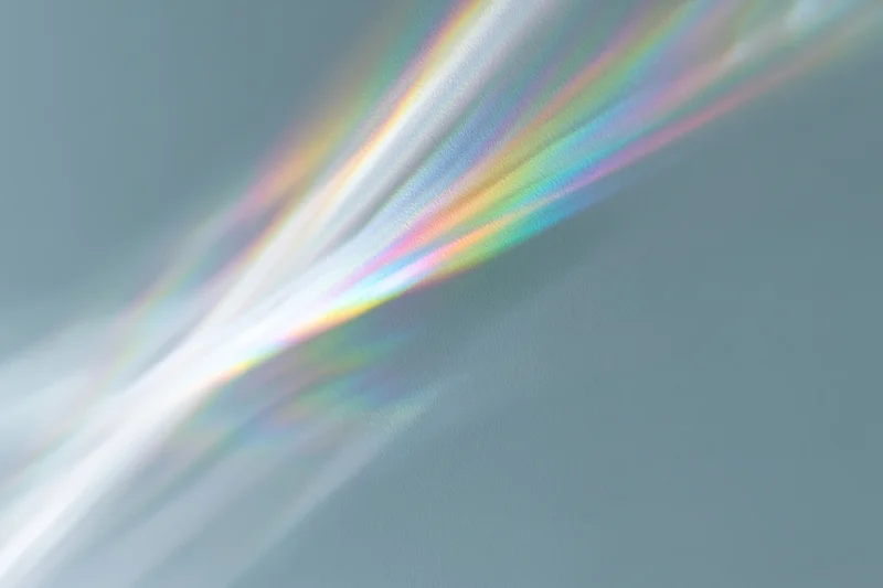 Rainbow light refraction cast across a pale grey-white wall surface