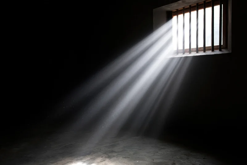 Rays of daylight streaming through a barred window in a prison cell interior