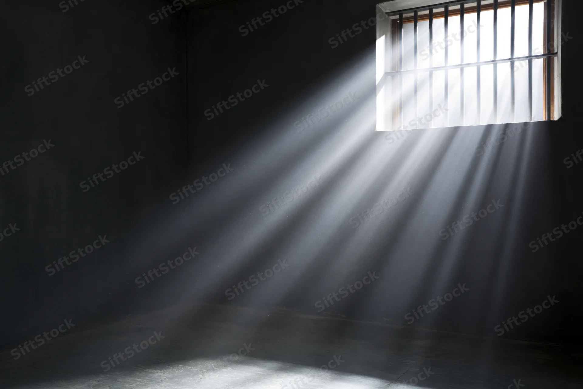 Sunlight streaming through a barred window in a dark prison cell