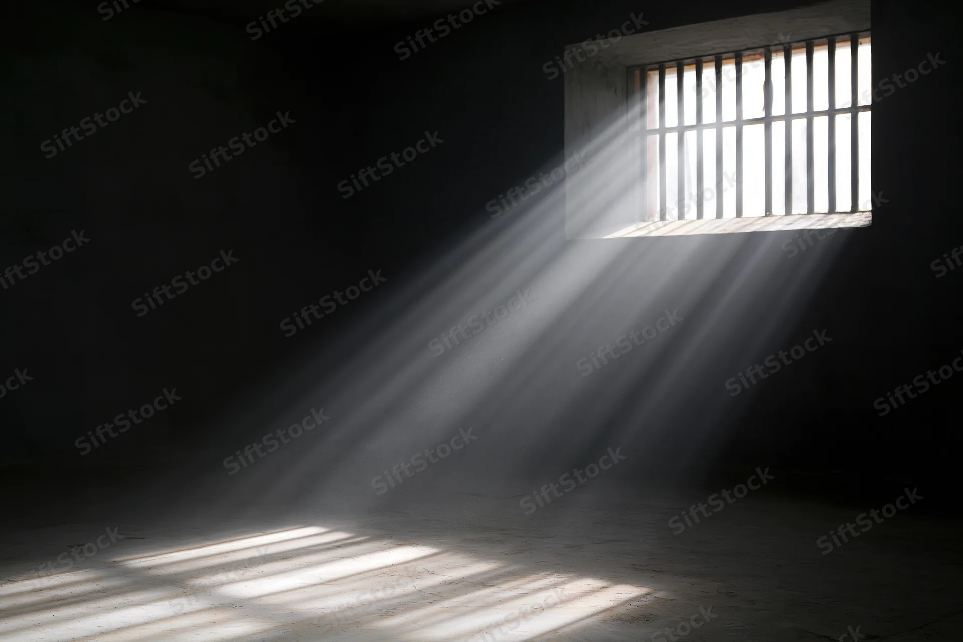 Sunlight streaming through a barred window in a prison cell interior