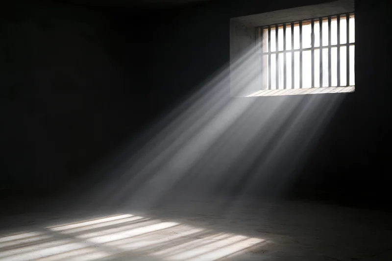 Sunlight streaming through a barred window in a prison cell interior