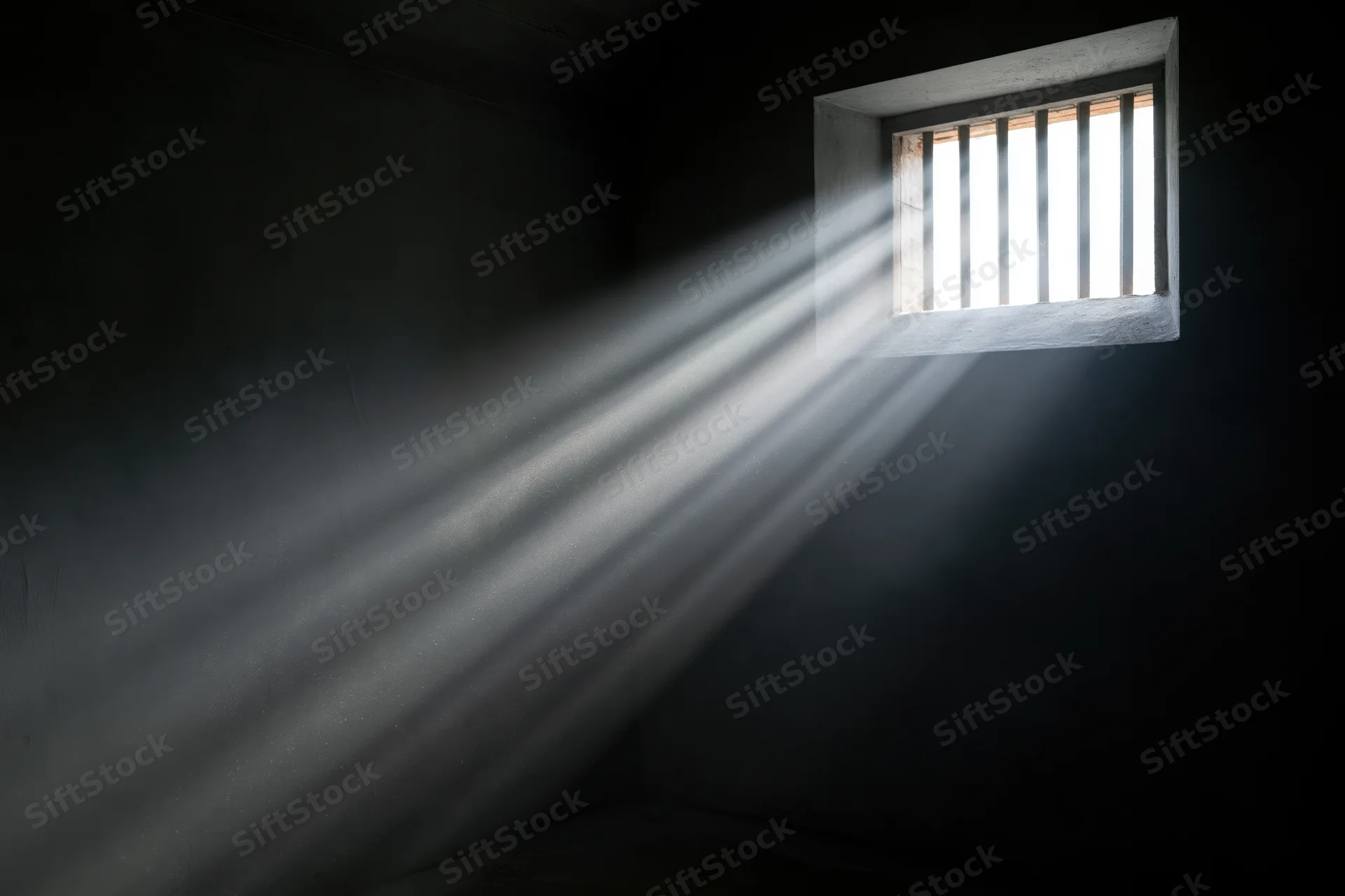Rays of daylight streaming through a small barred window in a dark prison cell