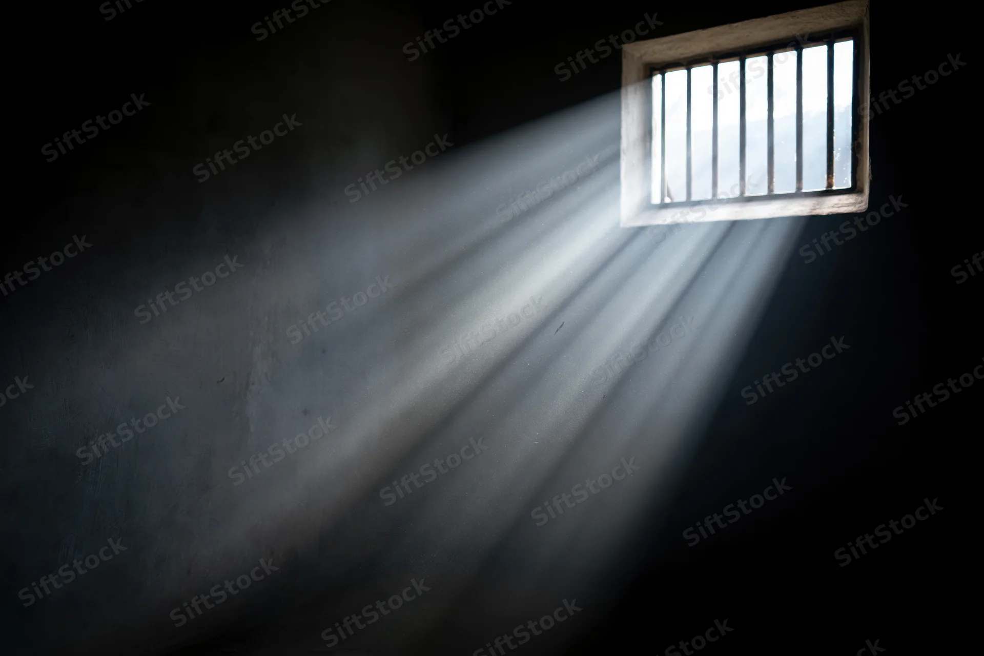 Rays of daylight streaming through a small barred window in a prison cell