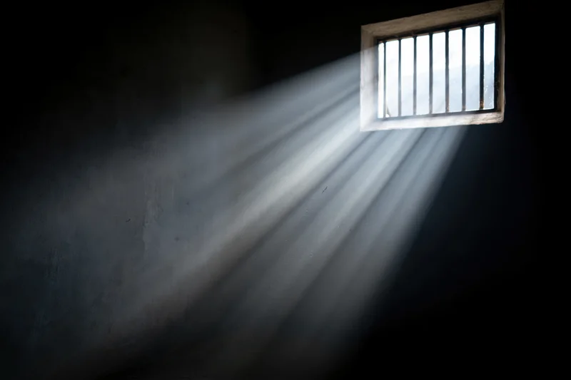 Rays of daylight streaming through a small barred window in a prison cell