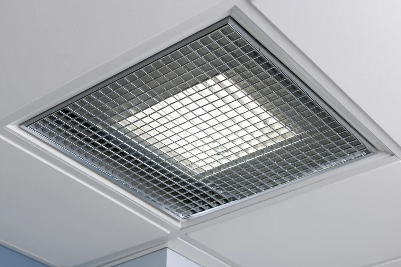 Recessed fluorescent ceiling light fixture with metal grid cover in office interior