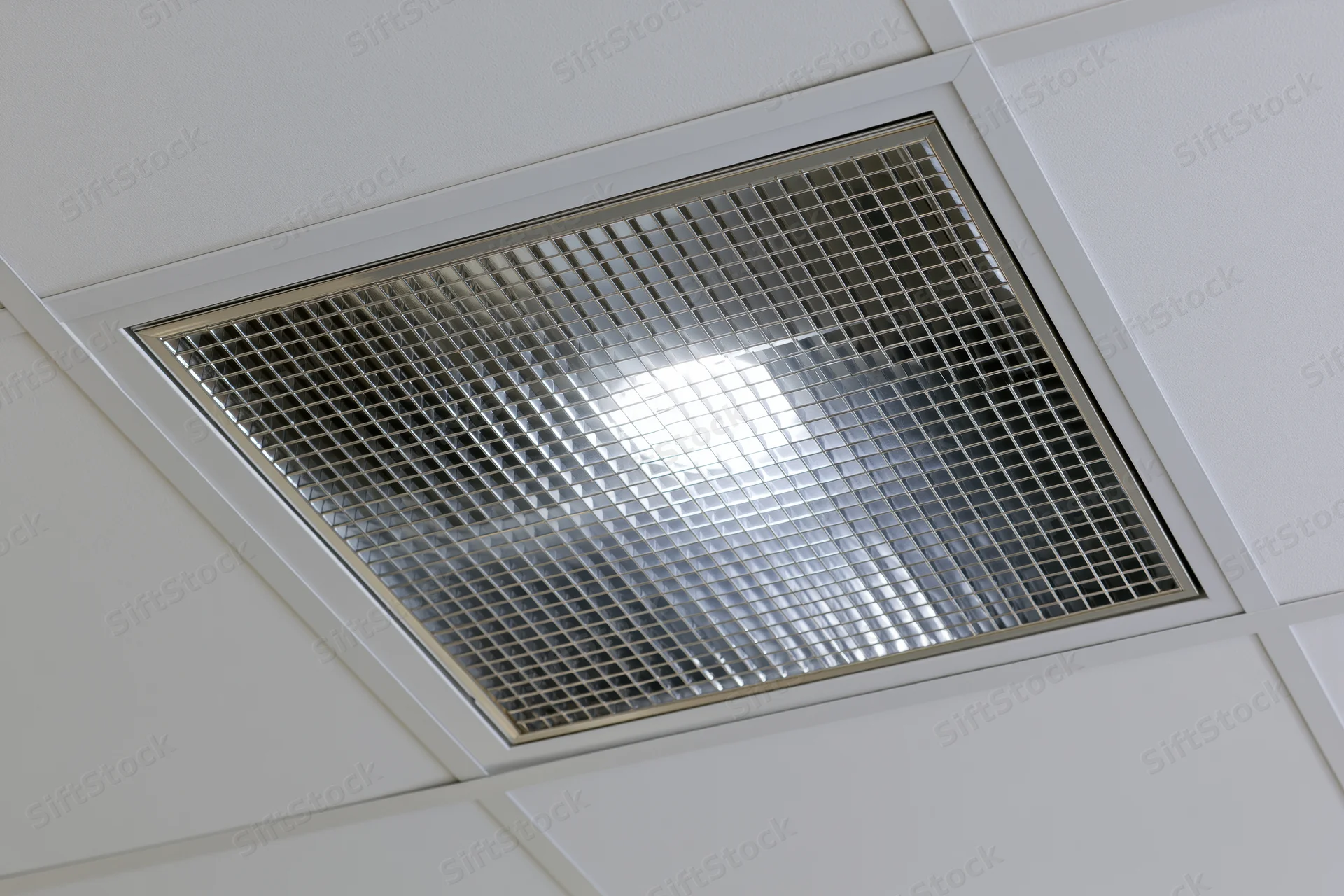 Recessed fluorescent ceiling light fixture with metal grid cover in office interior