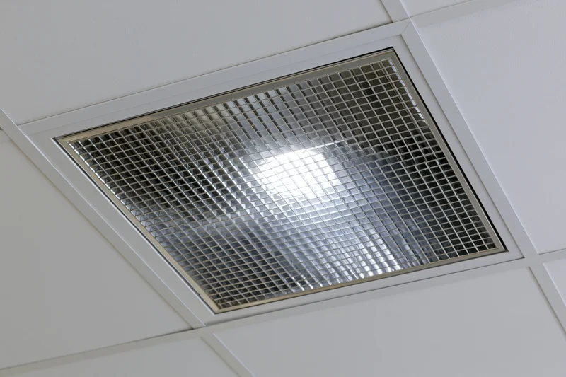 Recessed fluorescent ceiling light fixture with metal grid cover in office interior