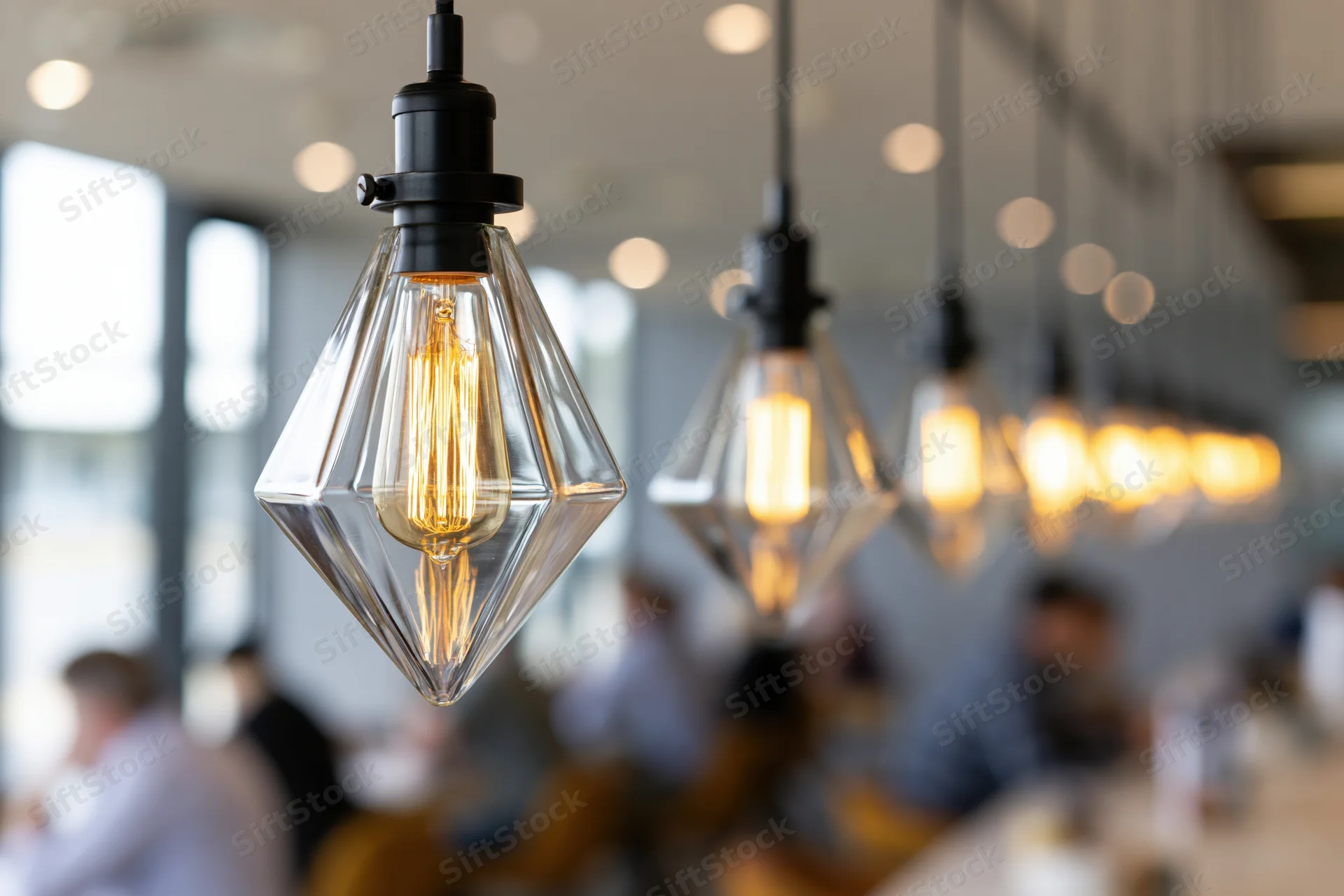 Row of geometric glass pendant lights hanging over dining tables in a restaurant interior