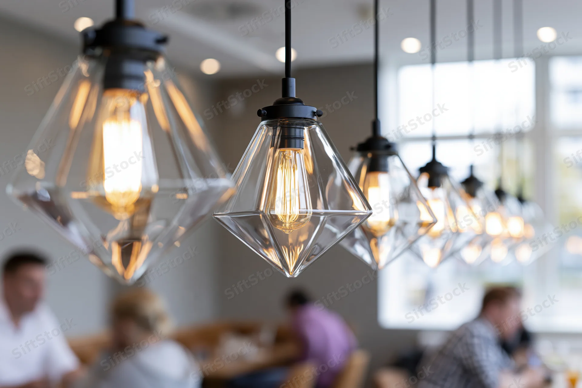 Row of geometric pyramid-shaped clear glass pendant lights hanging over dining area in restaurant with people seated at tables