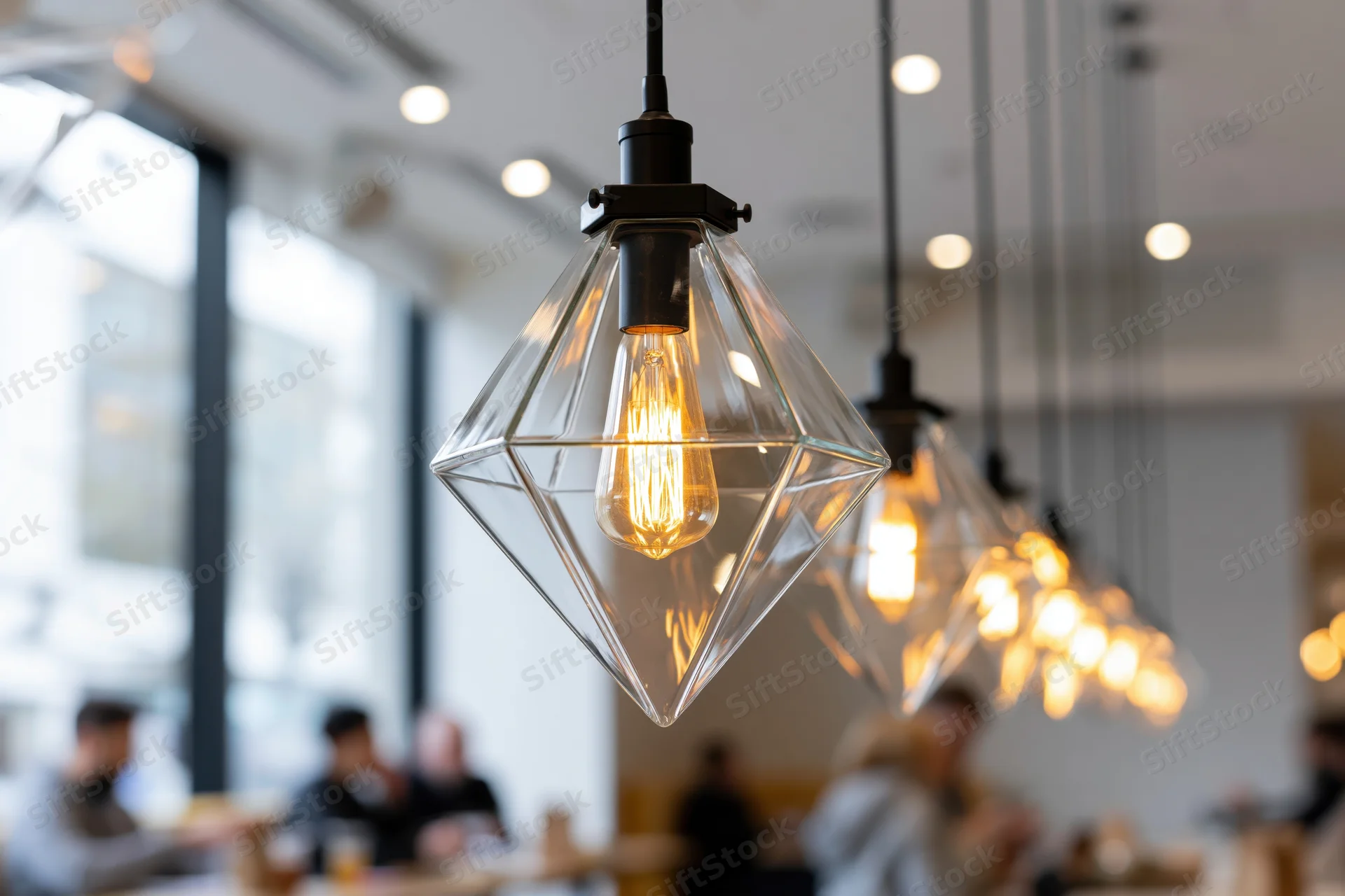 Row of geometric pyramid-shaped clear glass pendant lights with edison bulbs hanging in a modern cafe interior