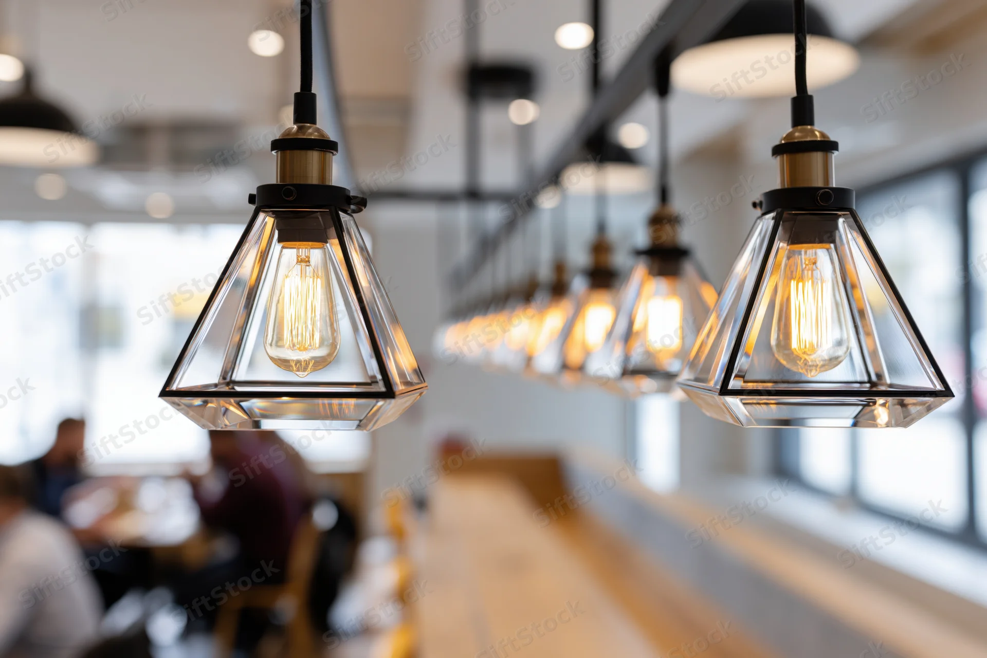 Row of triangular glass pendant lights with exposed filament bulbs hanging over a restaurant dining area