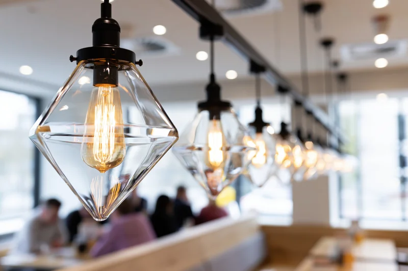 Row of geometric triangular glass pendant lights with exposed filament bulbs hanging over dining area in restaurant interior