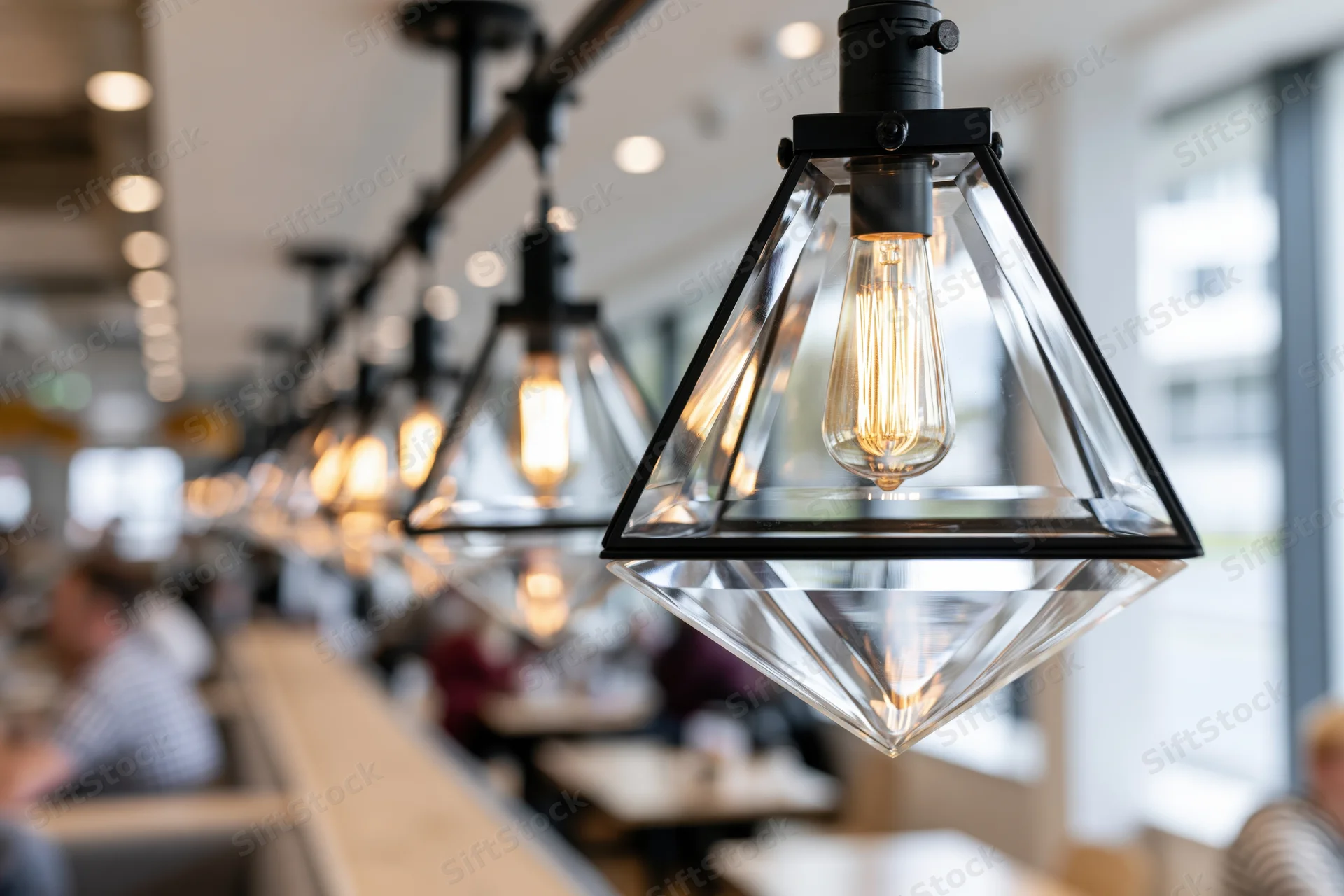 Row of triangular glass pendant lights with exposed filament bulbs hanging over dining tables in a restaurant interior