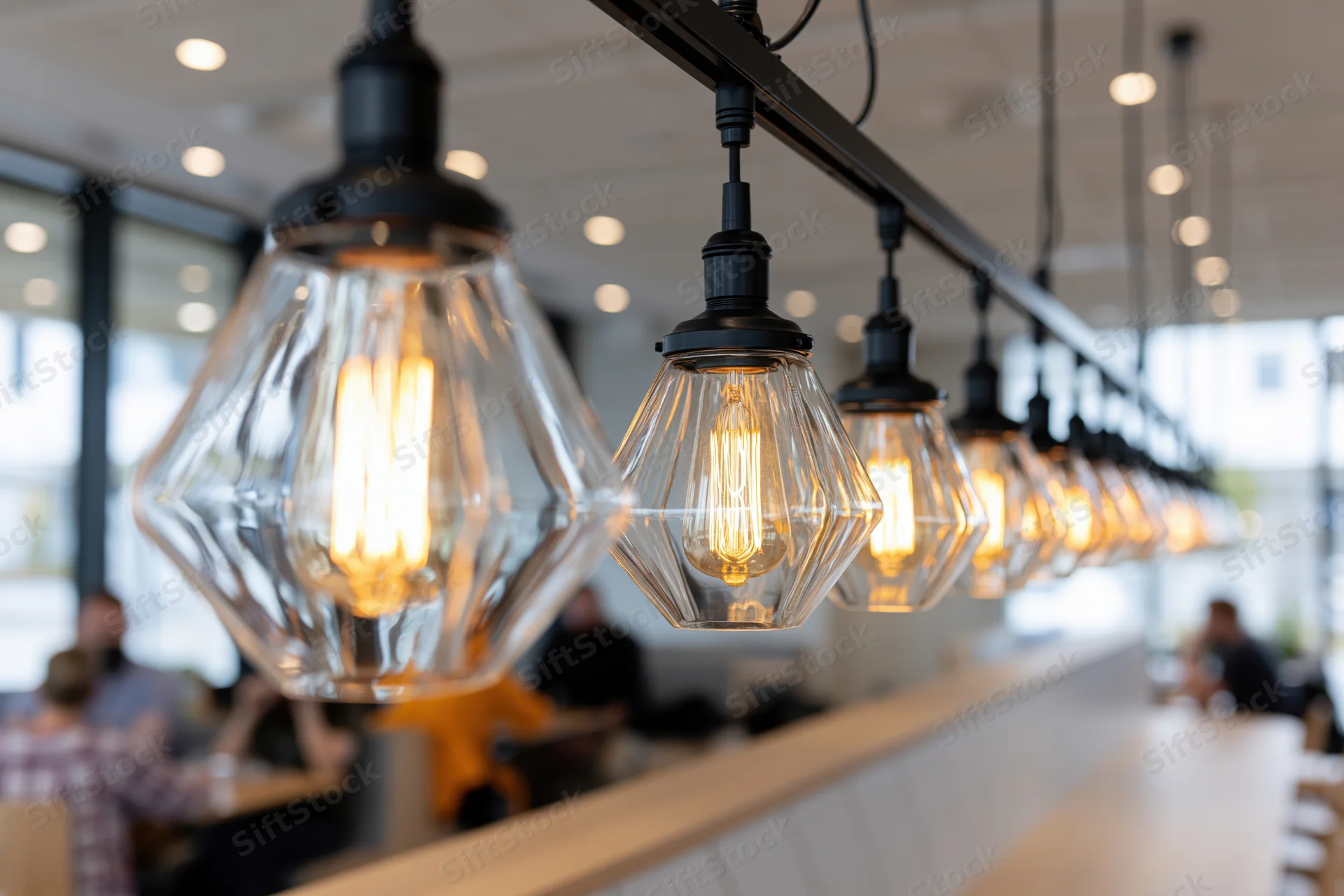 Row of geometric triangular glass pendant lights with exposed filament bulbs hanging over a wooden bar counter in a modern restaurant interior