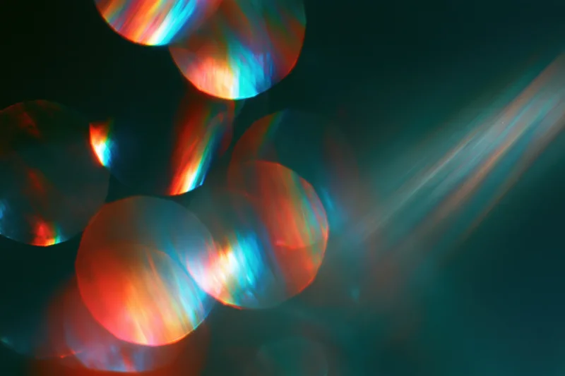 Scattered rainbow light refractions floating against a deep dark background