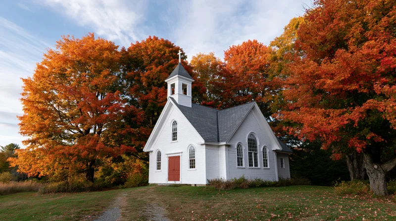 Small white clapboard church with steeple surrounded by autumn trees in rural countryside
