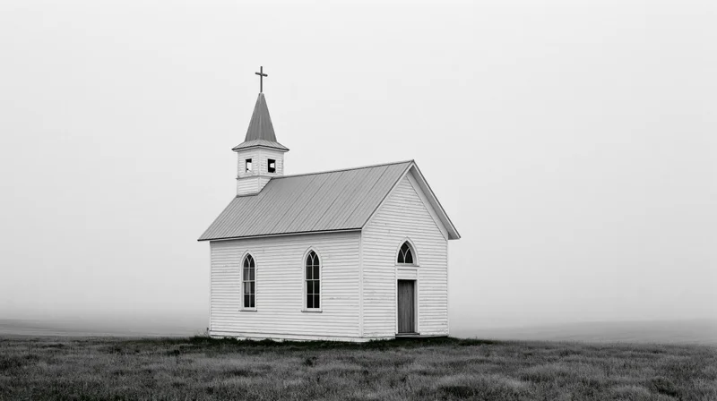 Small white clapboard church with steeple and cross on open prairie field