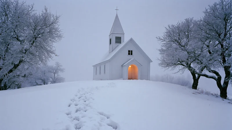 Small white country church with pointed steeple on snowy hill, entrance glowing warmly, path of footprints leading up to it