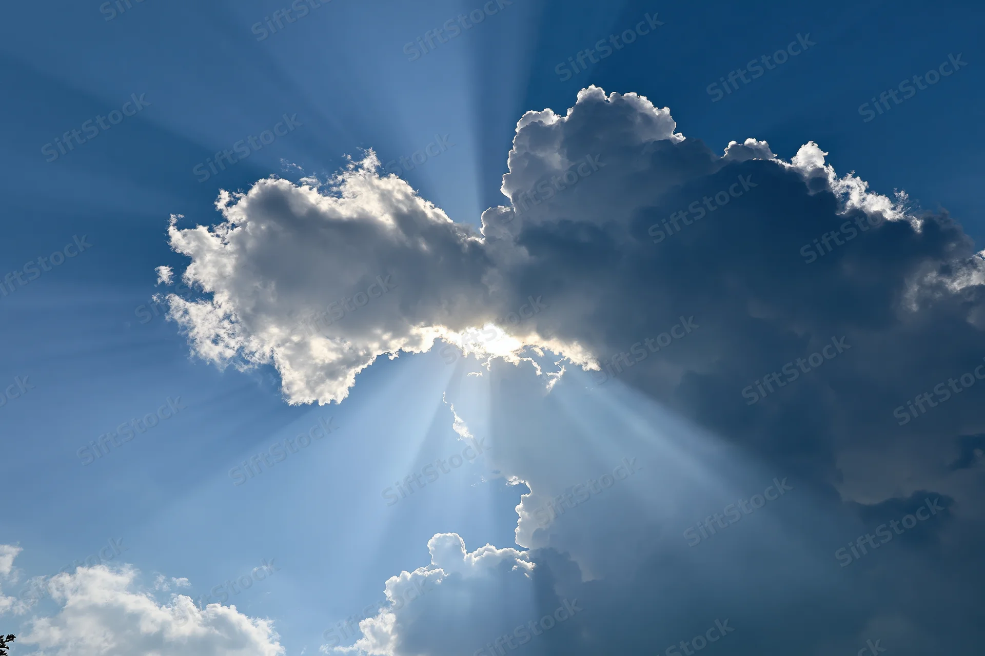 Sun breaking through gap in cumulus clouds sending rays across blue sky