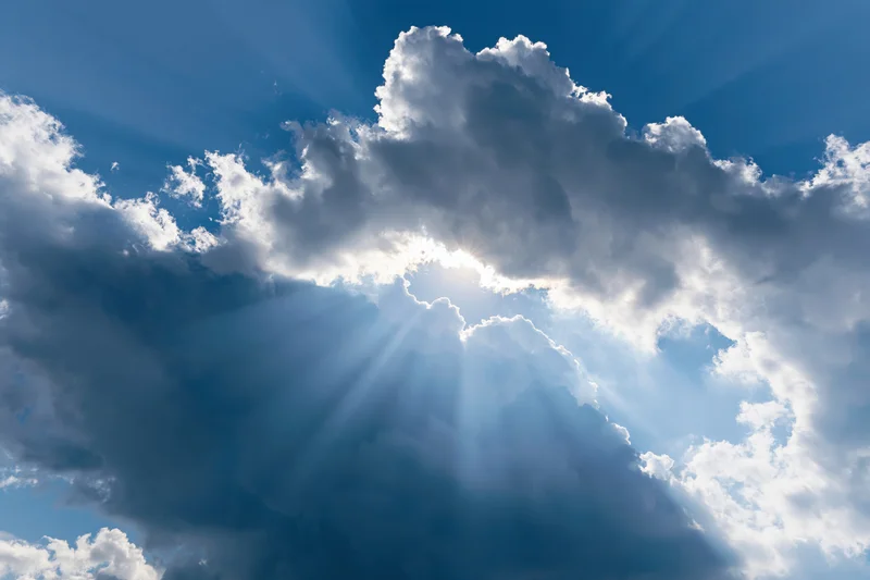 Sun breaking through cumulus clouds in a blue sky sending rays of light