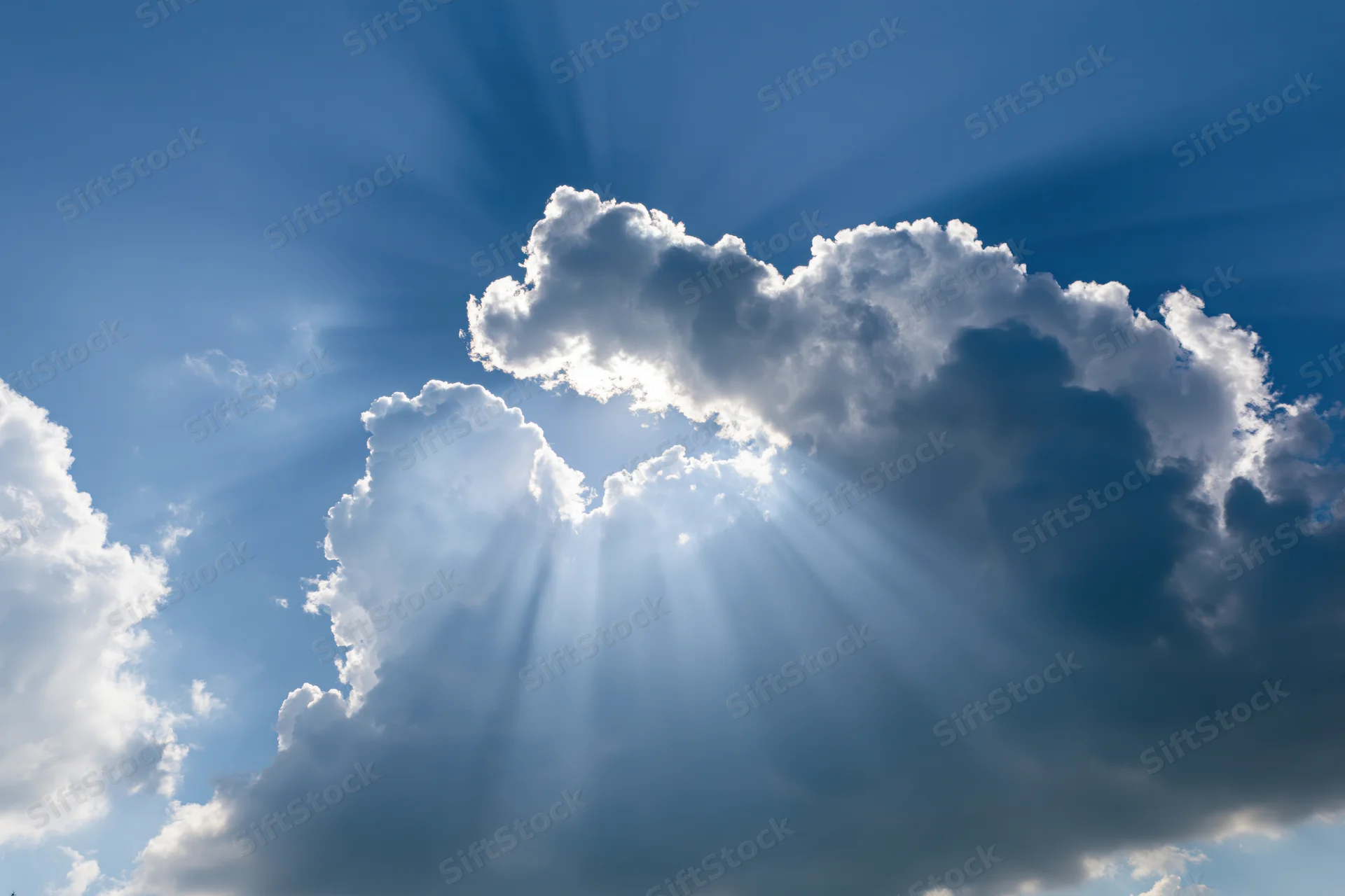 Sun breaking through cumulus clouds in a blue sky sending rays of light