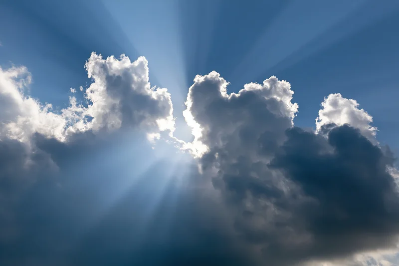 Sun breaking through cumulus clouds in a blue sky sending rays of light downward