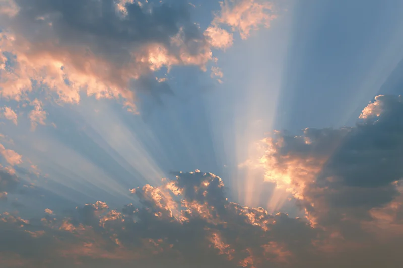 Sun rays breaking through layered clouds in an open sky