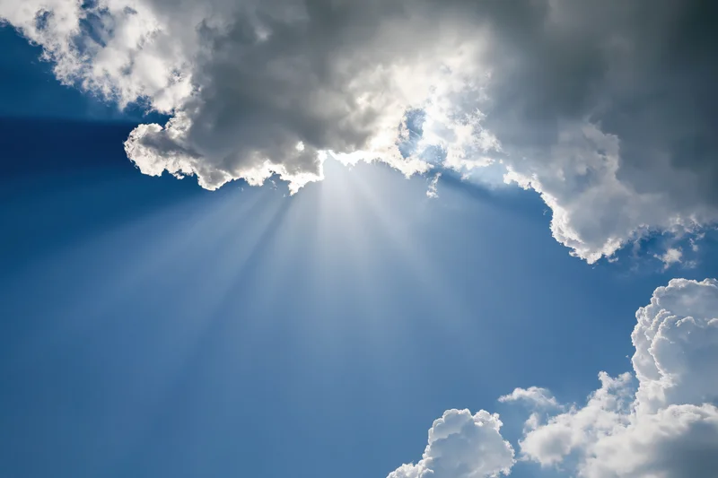 Sunlight breaking through dense cumulus clouds in a blue sky