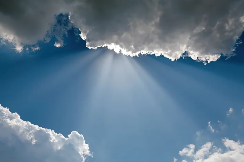 Sunlight breaking through dense cumulus clouds in a blue sky