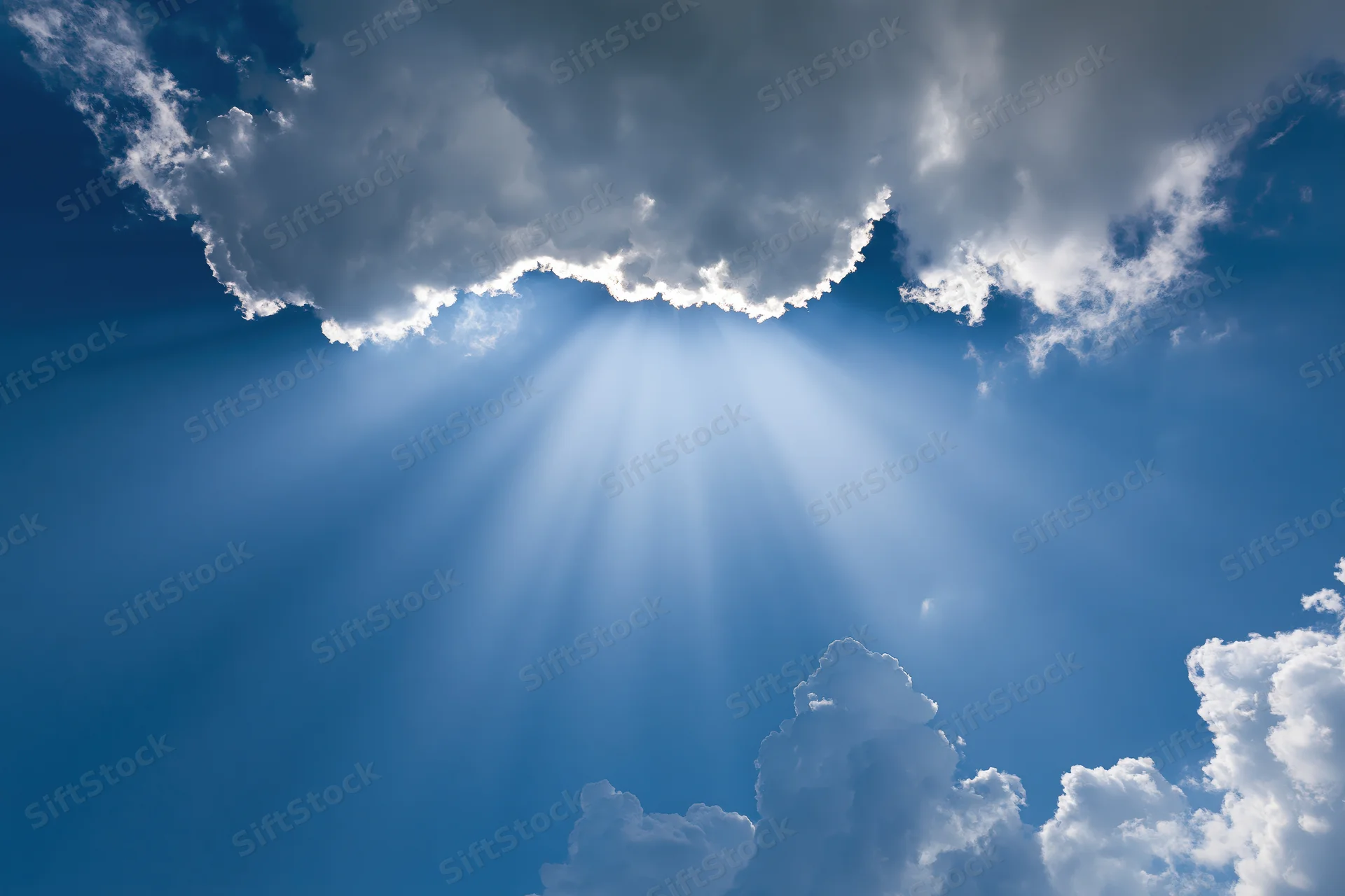 Sunlight breaking through dense cumulus clouds in a clear blue sky