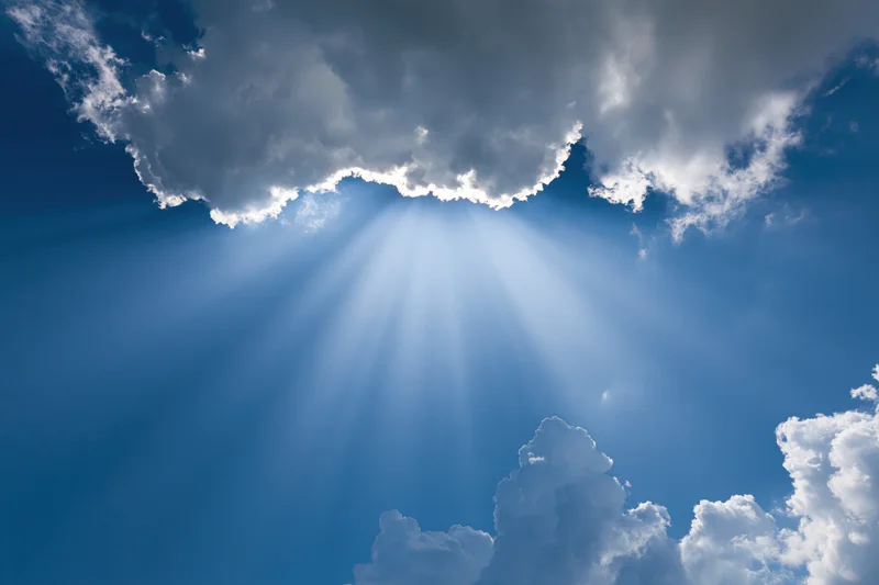 Sunlight breaking through dense cumulus clouds in a clear blue sky