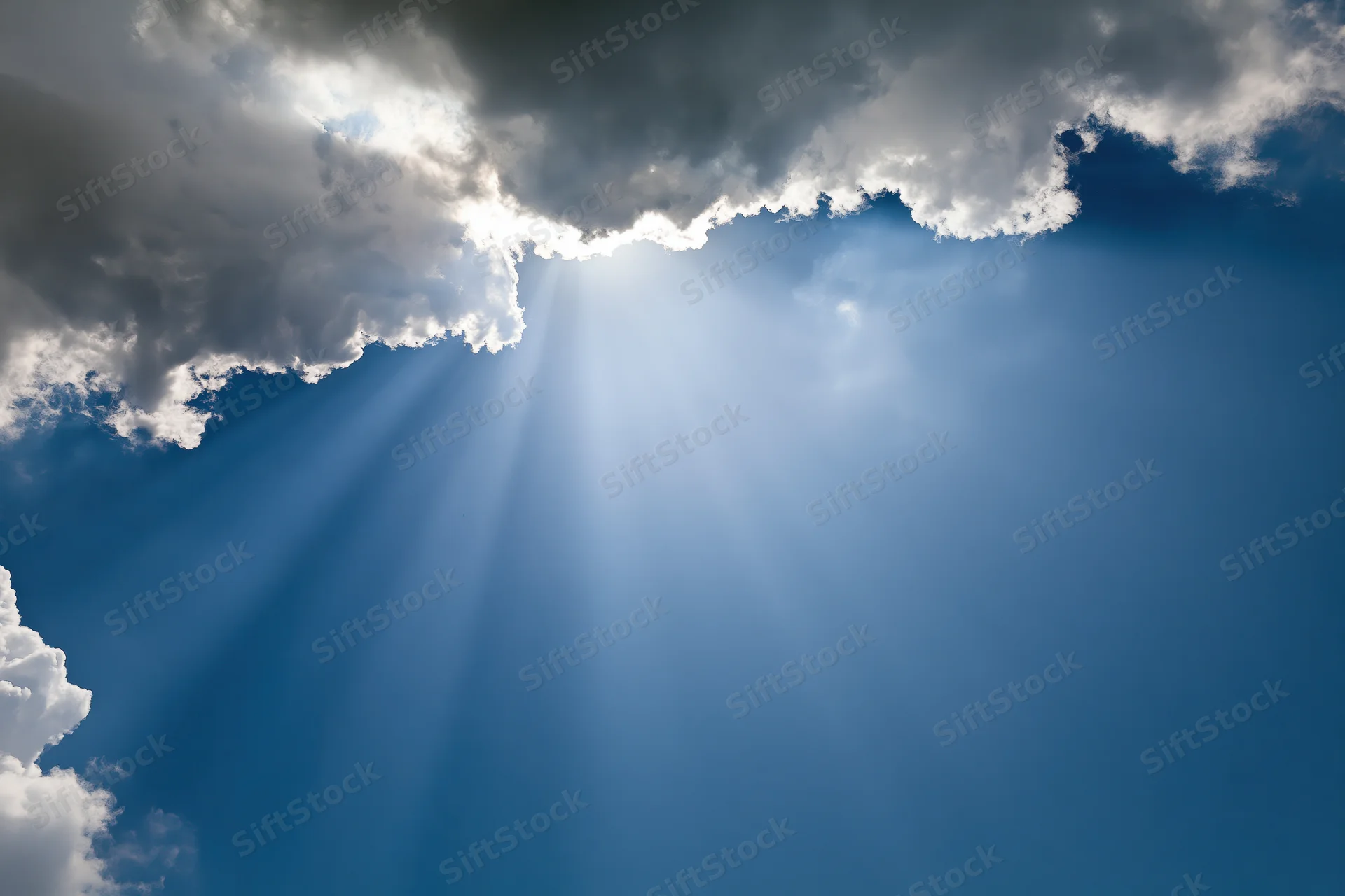Sunlight breaking through dense cumulus clouds in a blue sky
