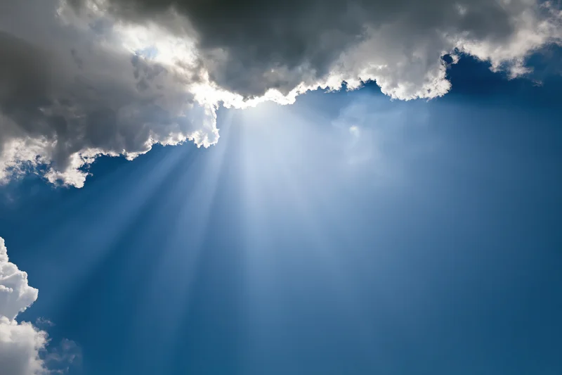Sunlight breaking through dense cumulus clouds in a blue sky