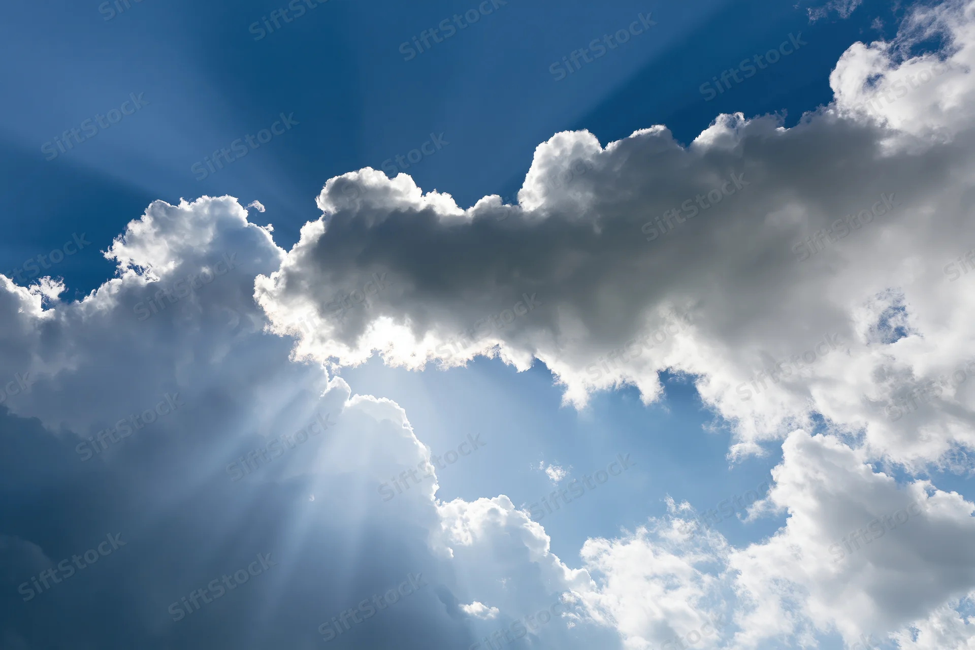 Sunlight breaking through dense white clouds in a blue sky