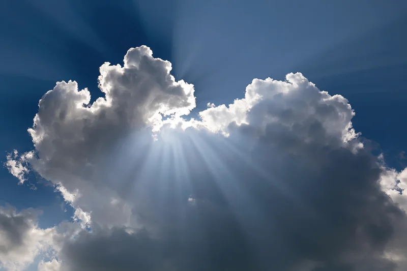 Sunlight breaking through dense clouds in a blue sky
