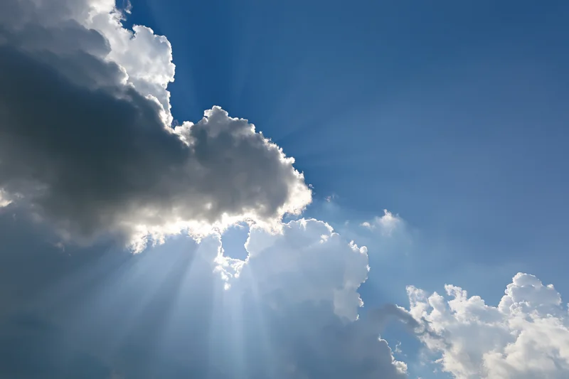 Sunlight breaking through dense clouds in a blue sky