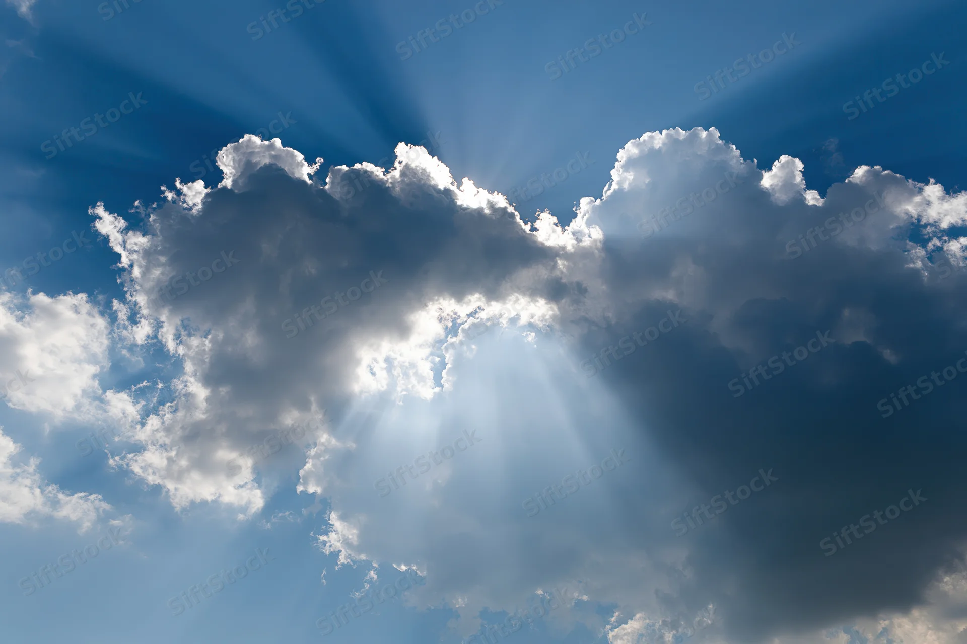 Sunlight breaking through dense cumulus clouds in a blue sky