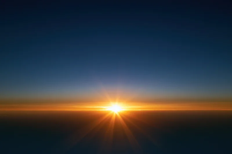 Sunrise light burst at horizon radiating golden rays upward across sky