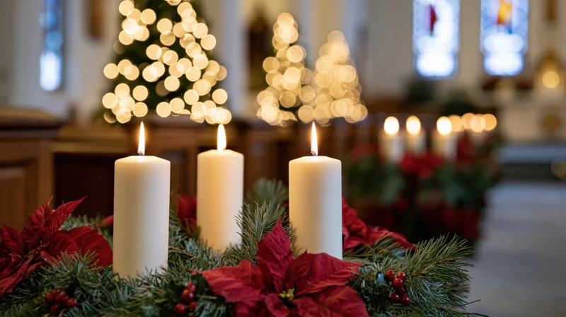 Three white candles burning in an advent wreath of pine and poinsettia inside a church with blurred holiday lights in the background