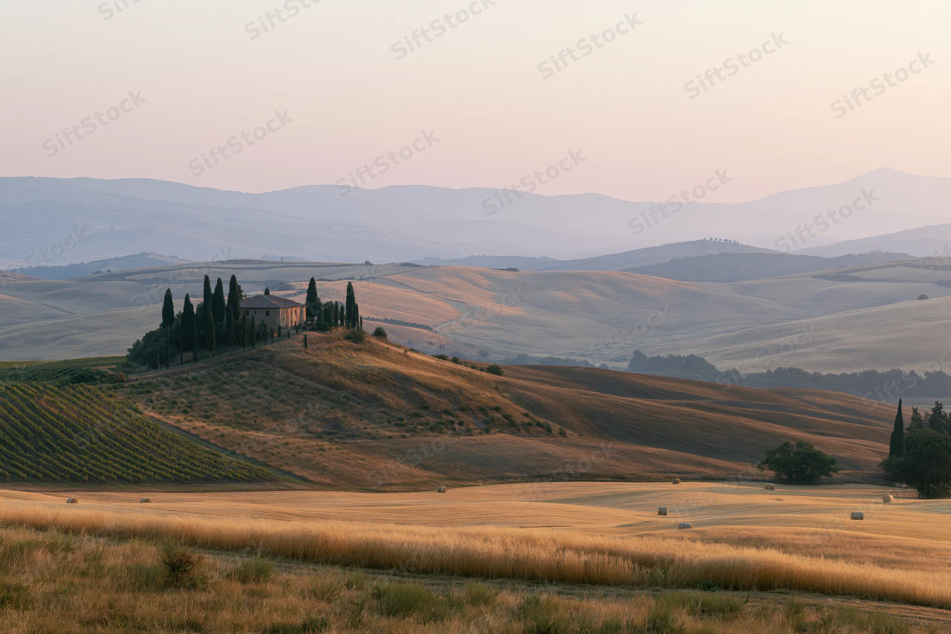 Stone farmhouse perched on a hill surrounded by vineyards and wheat fields in the tuscan countryside at sunset