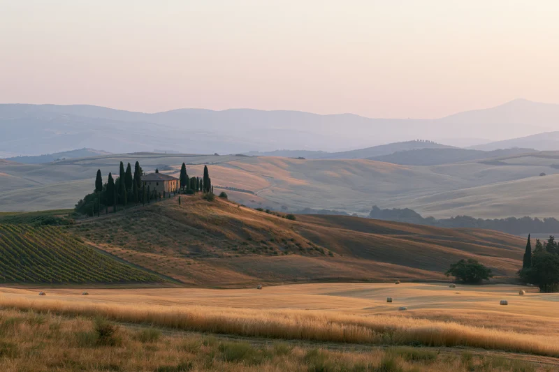 Stone farmhouse perched on a hill surrounded by vineyards and wheat fields in the tuscan countryside at sunset