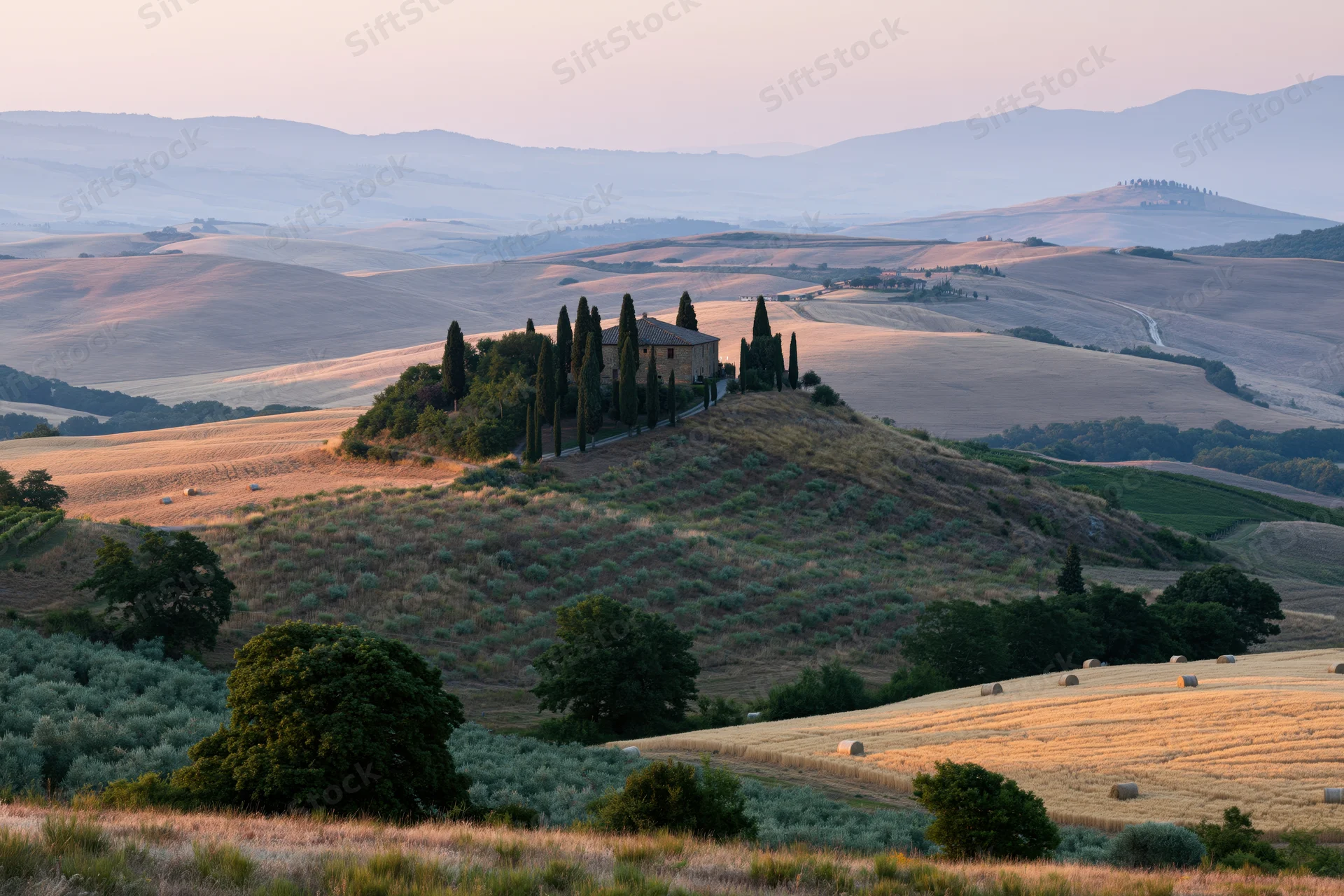 Stone farmhouse perched on a hill surrounded by fields and cypress trees in the tuscan countryside at sunset