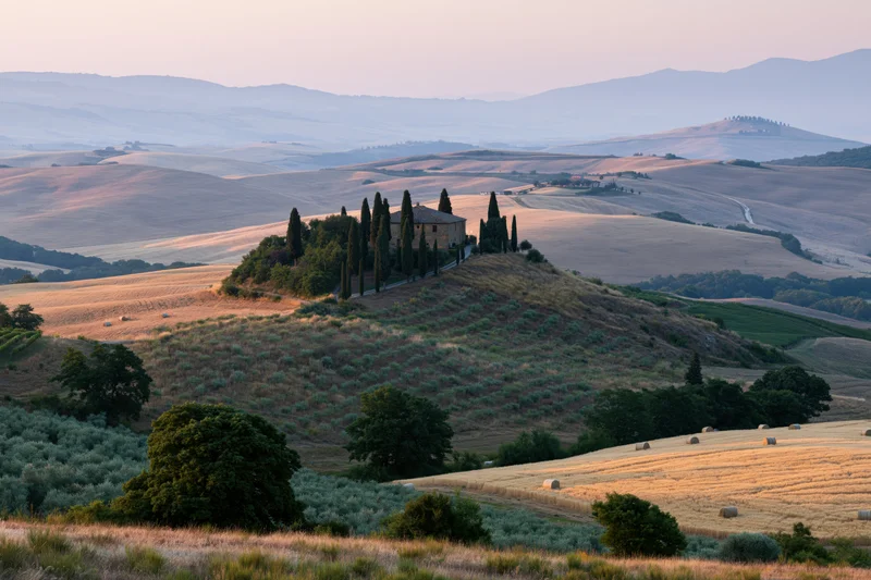 Stone farmhouse perched on a hill surrounded by fields and cypress trees in the tuscan countryside at sunset