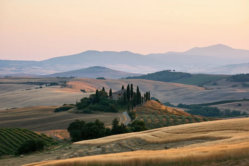 Stone farmhouse perched on a hill surrounded by golden fields and cypress trees in the tuscan countryside at sunset
