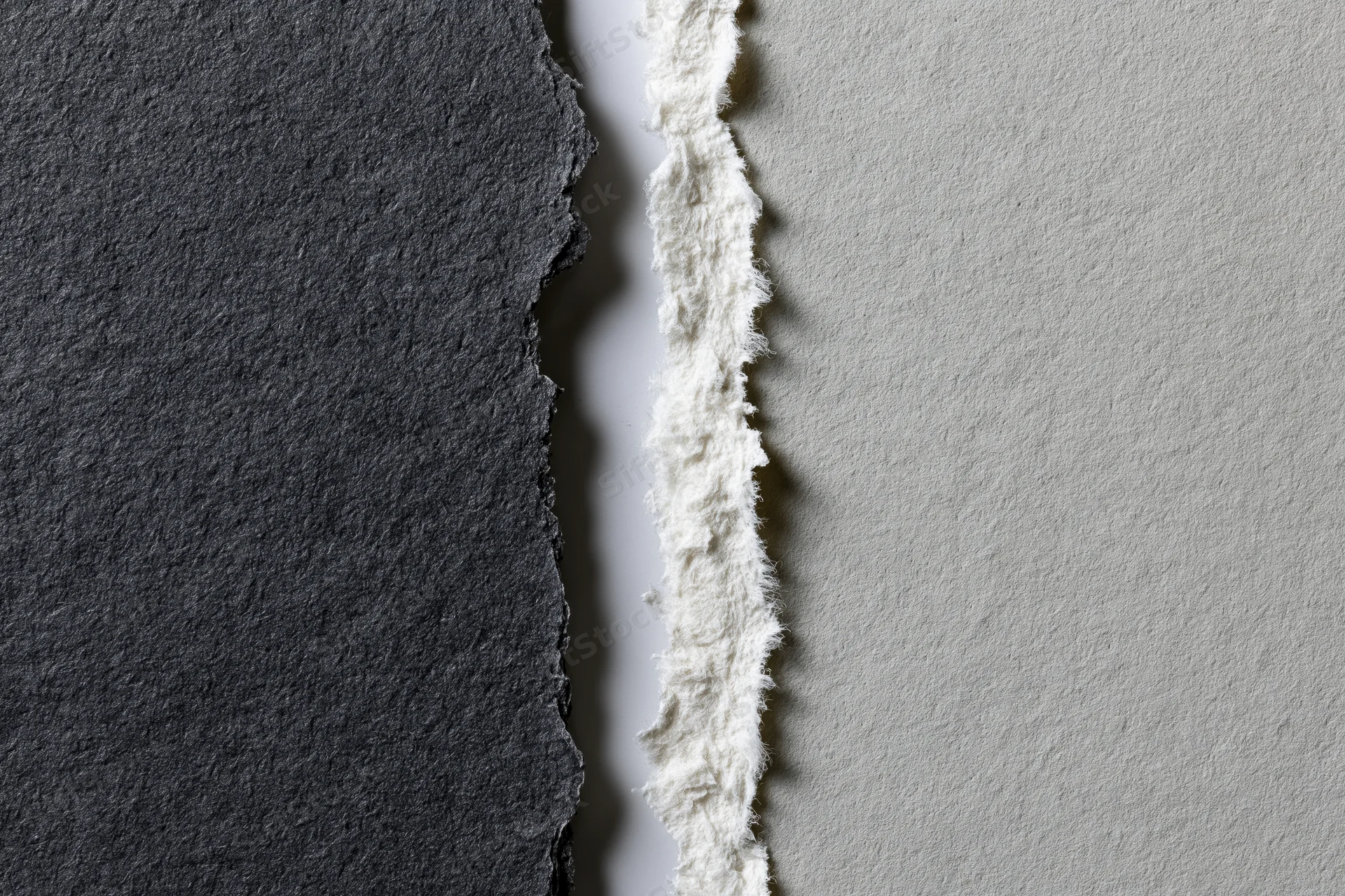 Two torn sheets of paper placed side by side with ragged edges and contrasting dark charcoal and light gray surfaces