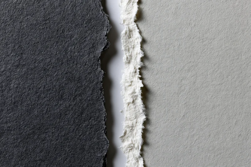 Two torn sheets of paper placed side by side with ragged edges and contrasting dark charcoal and light gray surfaces