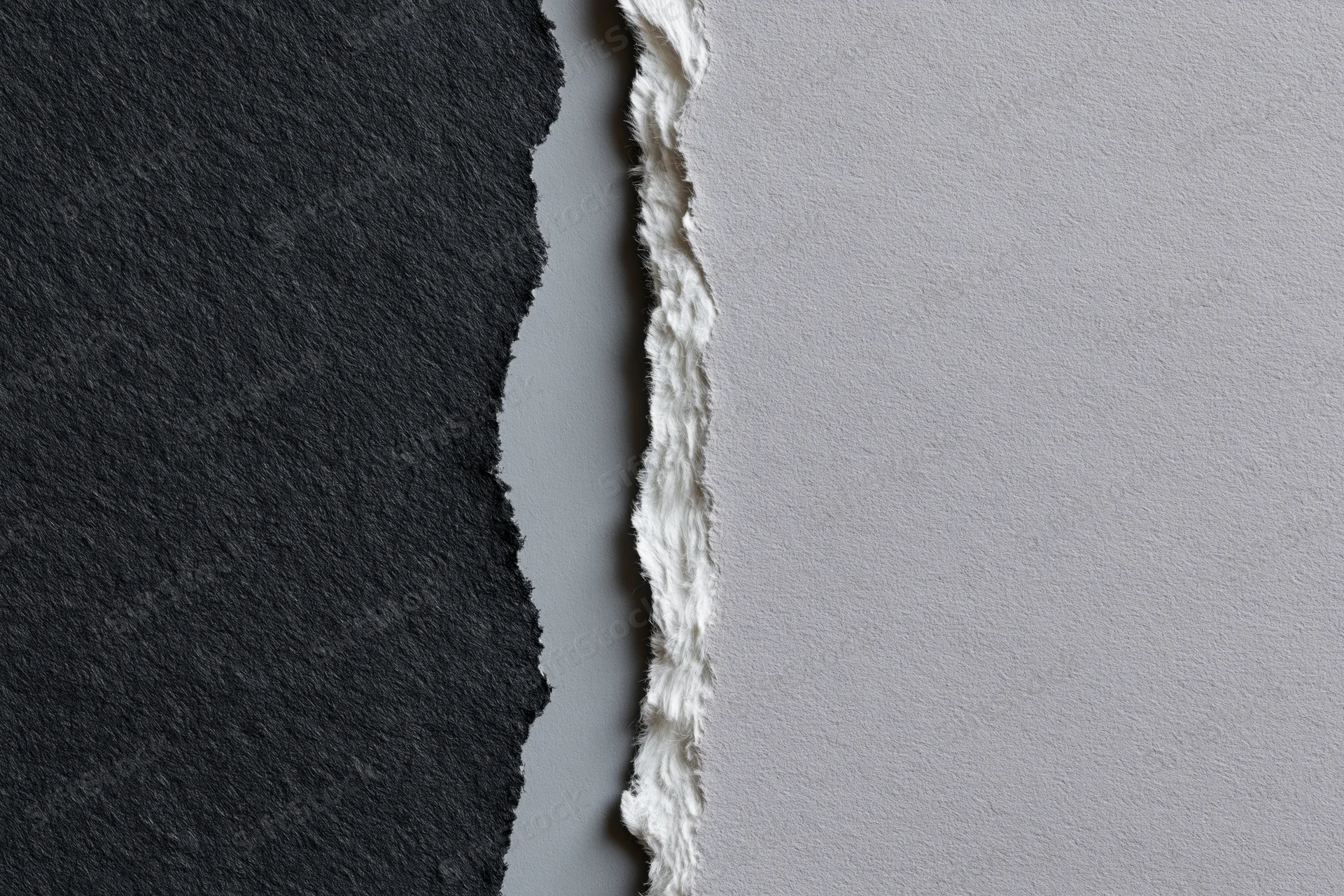 Two torn sheets of paper placed side by side with a jagged edge separating dark charcoal and light gray surfaces
