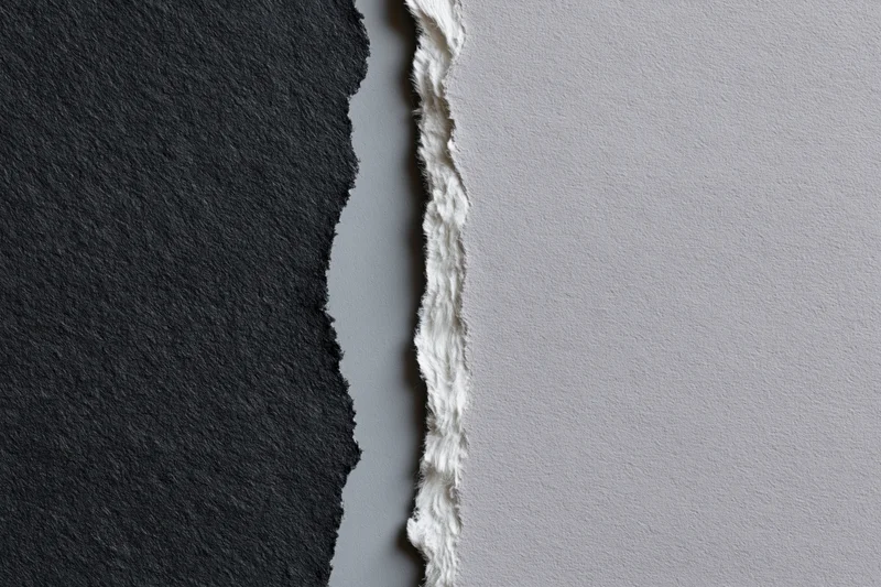 Two torn sheets of paper placed side by side with a jagged edge separating dark charcoal and light gray surfaces
